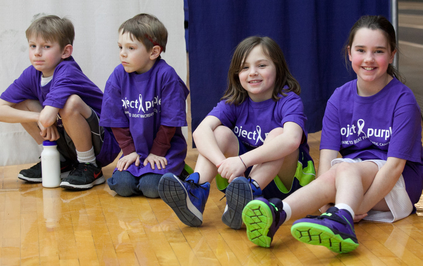 children on gym floor wearing Purple shirt with white project purple logo